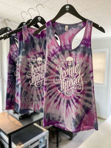Racerback tank top in a spirl tie dye pattern of Gray, pink, purple and black. The tank top is hanging on a line with other tank tops behind it.